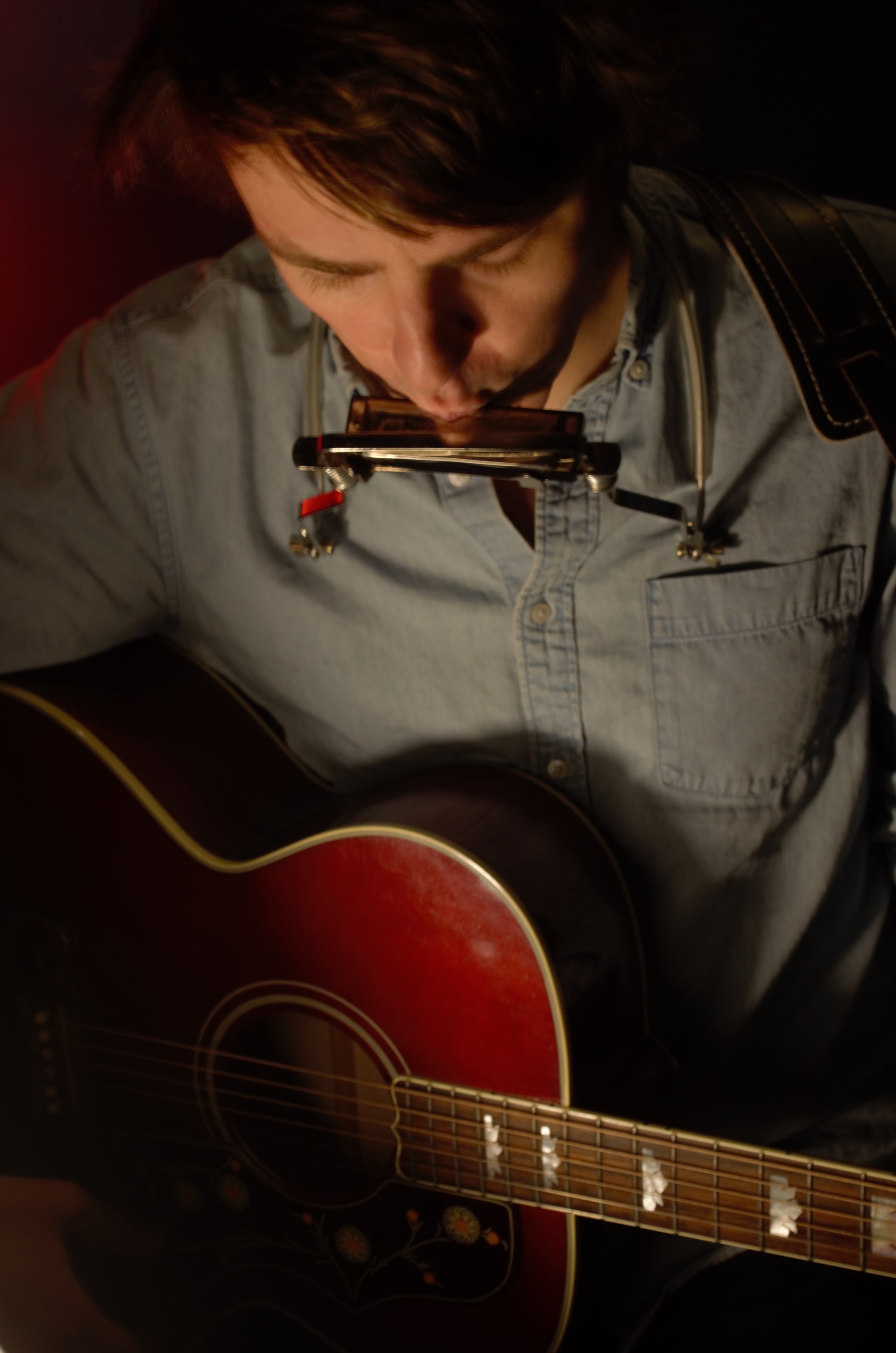 Trapper Schoepp playing the harmonica while holding his guitar